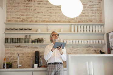 Geschäftsmann steuert Pendelleuchte in Cafeteria über digitales Tablet - RBF08311