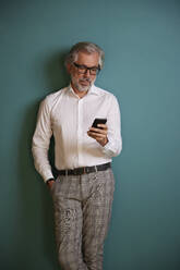 Male professional using mobile phone against green background - RBF08317