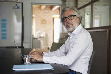 Male professional wearing eyeglasses working on laptop in office - RBF08319