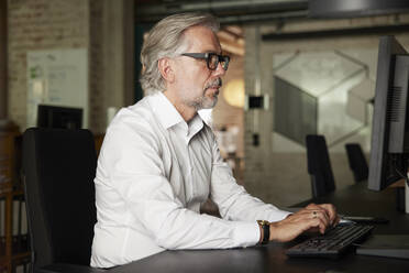 Geschäftsmann mit grauem Haar arbeitet am Computer im Büro - RBF08324