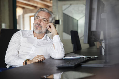 Nachdenklicher männlicher Berufstätiger mit grauem Haar sitzt am Schreibtisch im Büro - RBF08326