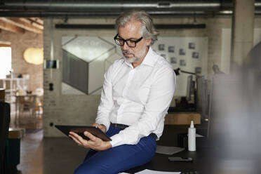 Male professional wearing eyeglasses working on digital tablet in office - RBF08330