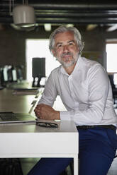 Mature male professional sitting with hands clasped at desk in office - RBF08333