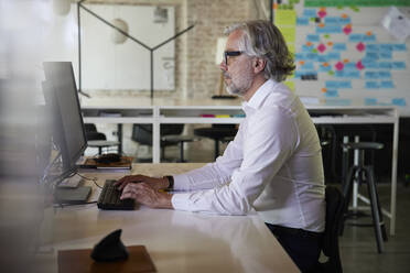 Mature businessman working on computer while sitting at desk in office - RBF08338