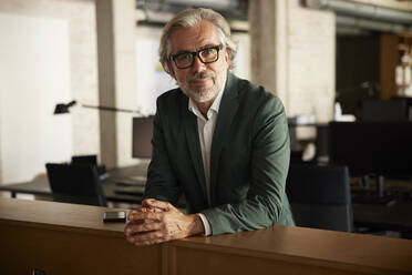 Male professional with hands clasped leaning on table in office - RBF08341