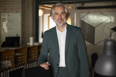 Elegant businessman by chair standing in office - RBF08345