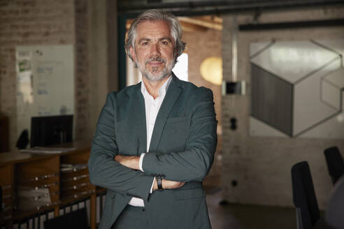 Confident male professional with arms crossed standing in office - RBF08346