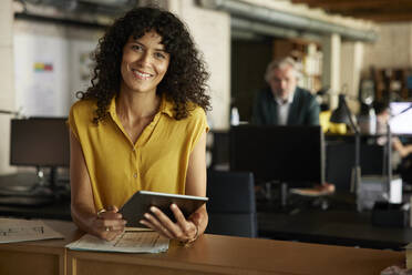 Smiling businesswoman with digital tablet leaning on table in office - RBF08361