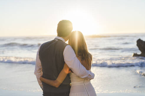 Junges frisch verheiratetes Paar mit Arm um Blick auf Sonnenaufgang Blick am Strand - AFVF09142