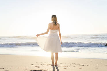 Young bride in wedding dress standing on beach - AFVF09147