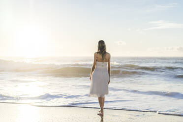 Bride looking at sunrise view while standing on beach - AFVF09149