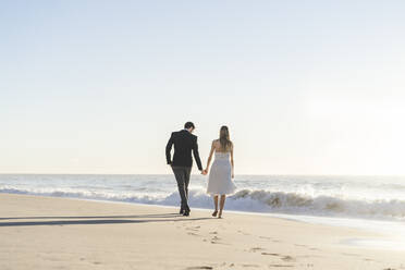 Neuvermähltes Paar, das am Strand spazieren geht und sich an den Händen hält - AFVF09150