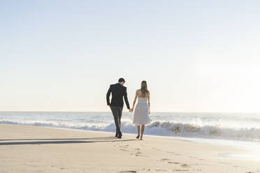 Newlywed couple holding hands while walking on beach - AFVF09150