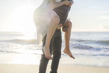 Young groom giving piggyback ride to bride at beach - AFVF09151