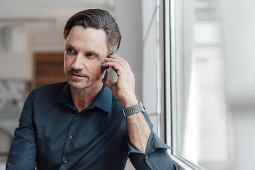 Mature businessman talking on smart phone at work place - JOSEF05487