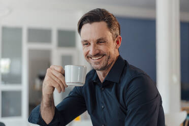 Smiling male professional having coffee in office - JOSEF05490