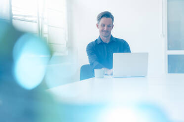 Smiling male professional working on laptop at desk in board room - JOSEF05494