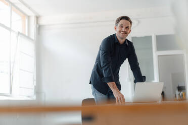 Lächelnd reifen männlichen Profi mit Laptop am Schreibtisch im Sitzungssaal im Büro - JOSEF05497