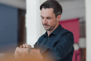 Älterer Geschäftsmann, der im Büro die Zeit auf seiner Armbanduhr überprüft - JOSEF05507