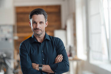 Businessman standing with arms crossed in office - JOSEF05509