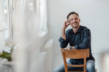 Smiling businessman contemplating while sitting on chair in office - JOSEF05528