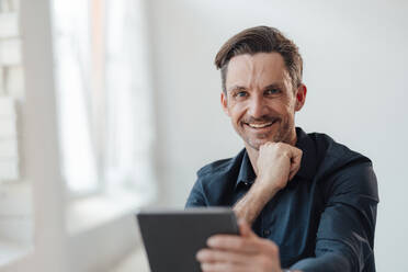 Lächelnder männlicher Fachmann, der ein digitales Tablet am Arbeitsplatz hält - JOSEF05530