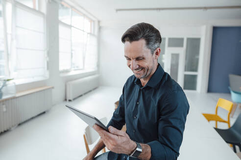 Lächelnde männliche Fachkraft bei der Arbeit an einem digitalen Tablet im Büro - JOSEF05535