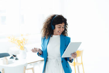 Lächelnde Geschäftsfrau mit Kopfhörern, die ein digitales Tablet im Büro benutzt - JOSEF05555