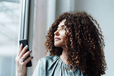 Geschäftsfrau schaut durch Glas und hält ein Smartphone - JOSEF05571