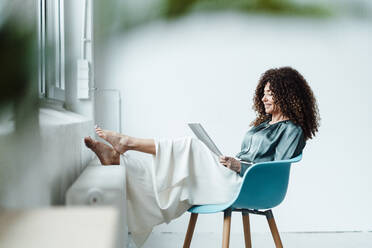 Businesswoman reading documents while sitting on chair in office - JOSEF05575