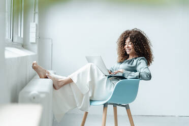 Businesswoman using laptop while sitting on chair in office - JOSEF05578