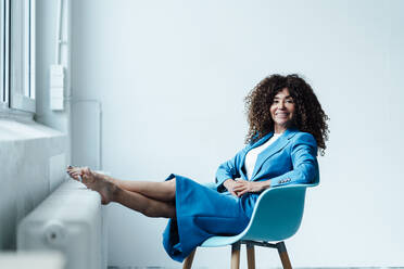 Lächelnde weibliche Geschäftsperson auf einem Stuhl im Büro sitzend - JOSEF05588
