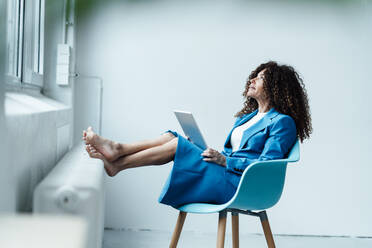 Reife Geschäftsfrau mit Laptop, die auf einem Stuhl sitzt und nach oben schaut - JOSEF05590