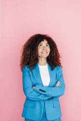 Businesswoman with arms crossed looking up against pink background - JOSEF05591