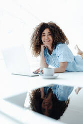 Smiling female professional with hand on chin lying on table in office - JOSEF05621