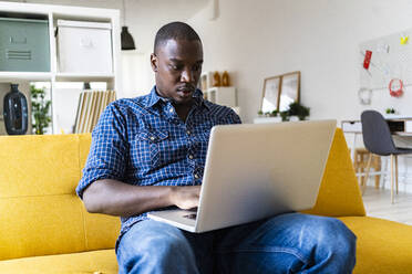Mann benutzt Laptop, während er zu Hause auf dem Sofa sitzt - GIOF13355