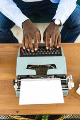 Mid adult man using old typewriter on table at home - GIOF13376