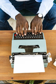 Mittlerer Erwachsener mit alter Schreibmaschine auf dem Tisch zu Hause - GIOF13376
