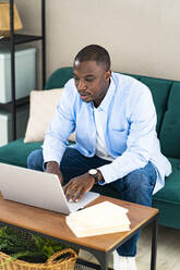 Male business person using laptop while sitting on sofa at home - GIOF13381