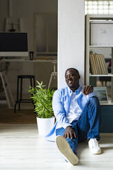 Smiling man sitting in front of column at home - GIOF13396