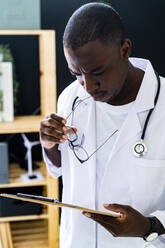 Thoughtful male doctor reading clipboard in medical clinic - GIOF13407