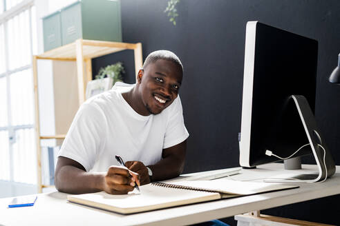 Smiling male freelance worker sitting at desk in studio - GIOF13416