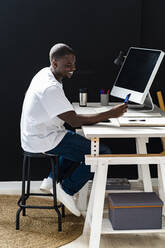 Glücklicher männlicher Freiberufler, der sein Smartphone benutzt, während er auf einem Hocker im Studio sitzt - GIOF13422