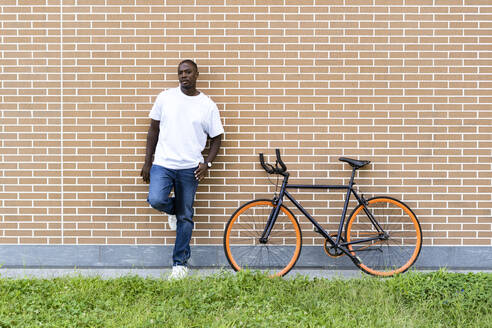 Mann mit Fahrrad vor einer Backsteinmauer stehend - GIOF13423