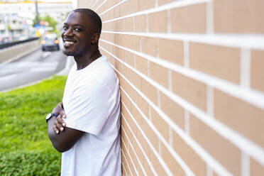 Happy mid adult man standing with arms crossed by brick wall - GIOF13428