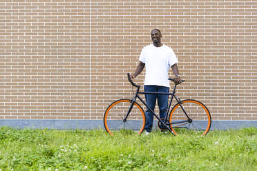 Mann mit Fahrrad vor einer Backsteinmauer stehend - GIOF13429