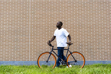 Mann, der ein Fahrrad vor einer Backsteinmauer fährt - GIOF13430