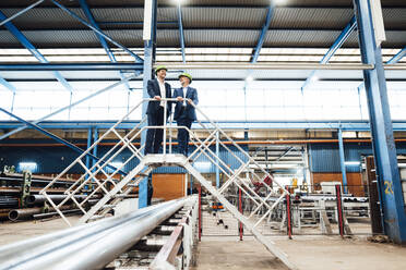 Male professionals discussing while standing on staircase in industry - JOSEF05636