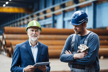 Male manager with digital tablet standing by warehouse worker in factory - JOSEF05703