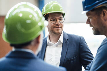 Male professionals looking at coworker discussing at warehouse - JOSEF05706